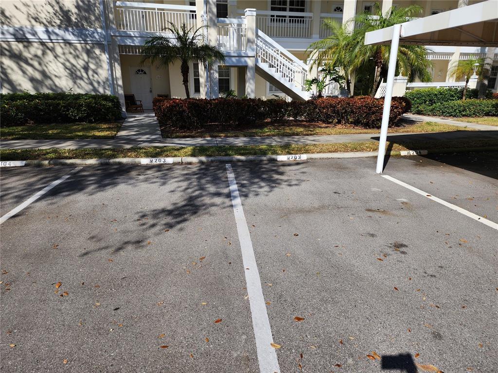 An outdoor parking area with numbered spaces sits in front of a multi-story residential building — 3701 54TH DRIVE W UNIT M203, BRADENTON, FL
