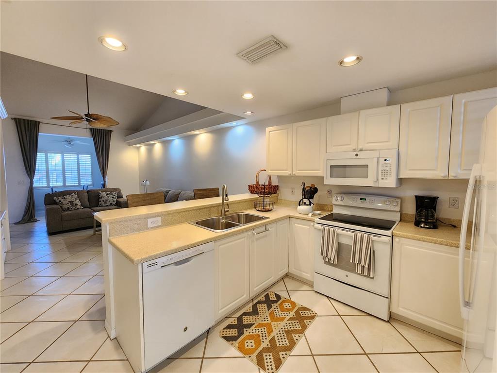 A kitchen with white cabinets, light countertops, and tile flooring opens into a living area — 3701 54TH DRIVE W UNIT M203, BRADENTON, FL