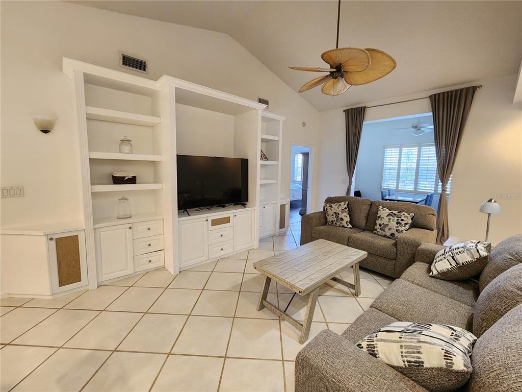 A living room features a large white built-in entertainment center, tile flooring, and two sofas — 3701 54TH DRIVE W UNIT M203, BRADENTON, FL