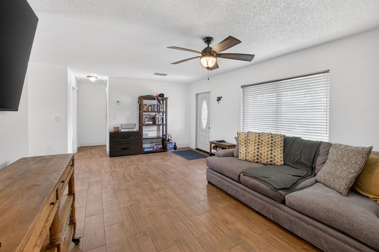 A living room features wood-look tile flooring, a grey sofa, a ceiling fan, and bookshelves — 9734 Alaska Circle, Boca Raton FL 33434, BOCA RATON, FL