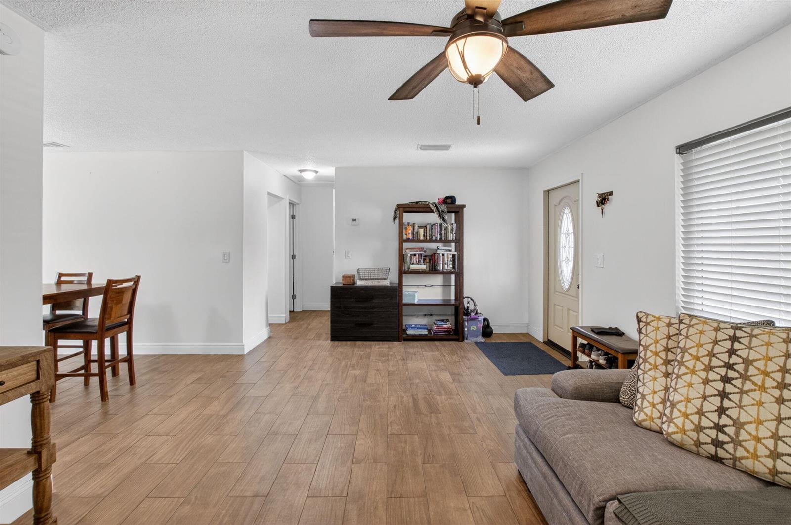 A living room with wood-look tile flooring, a ceiling fan, and a bookshelf near the door — 9734 Alaska Circle, Boca Raton FL 33434, BOCA RATON, FL