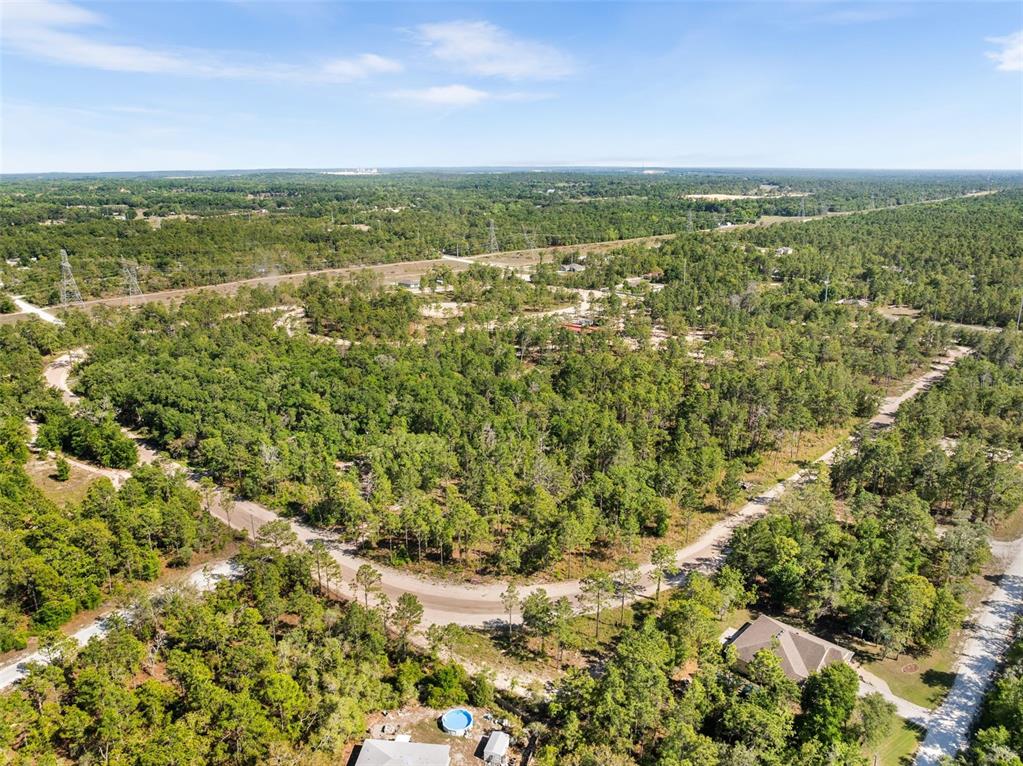 An aerial view shows a wooded residential area with dirt roads and scattered houses — 25723 BAREVA ROAD, WEEKI WACHEE, FL