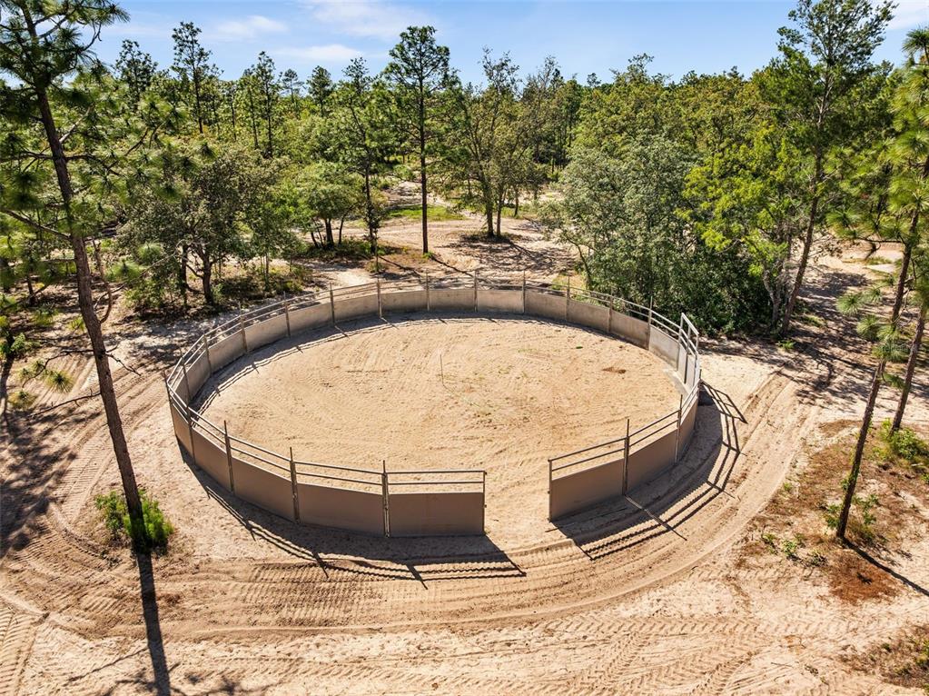 An aerial view of a circular horse training pen with metal fencing in a wooded area — 25723 BAREVA ROAD, WEEKI WACHEE, FL