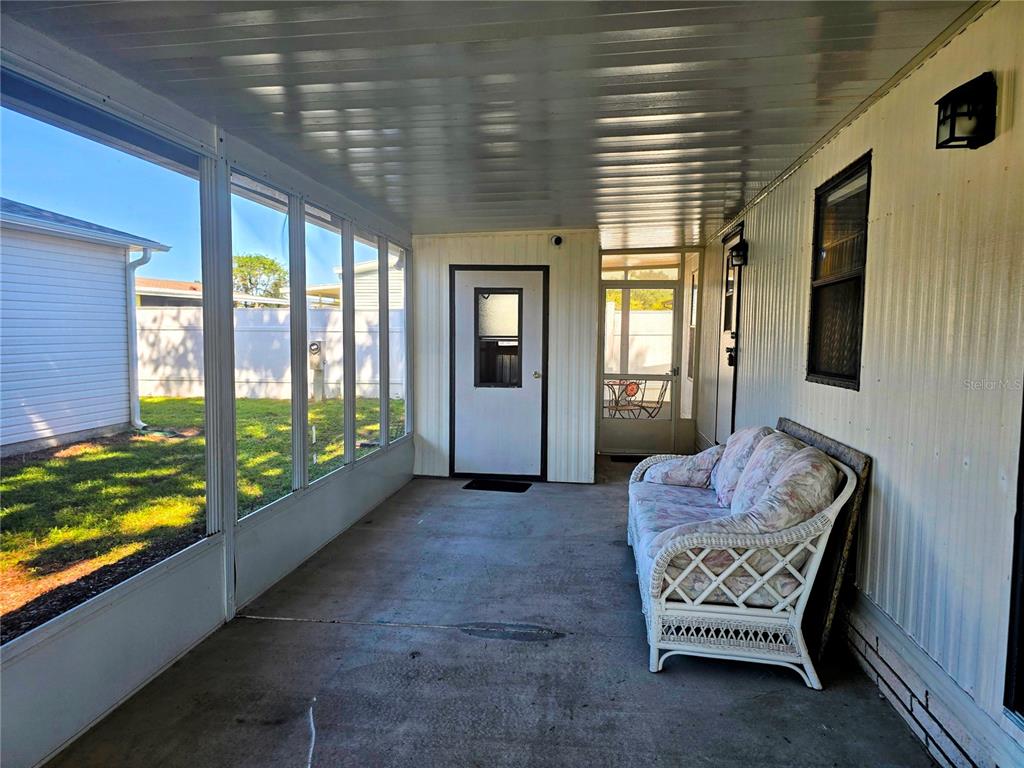 A covered porch features a concrete floor, screened walls, and a white wicker sofa — 615 NE COTTAGE PARK LANE, LEESBURG, FL
