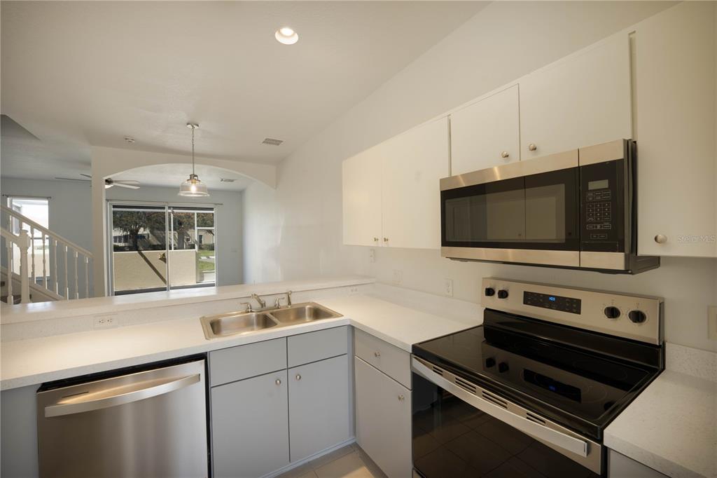 A kitchen with white cabinets, stainless steel appliances, and a view into the living area — 1241 S BEACH CIRCLE, KISSIMMEE, FL
