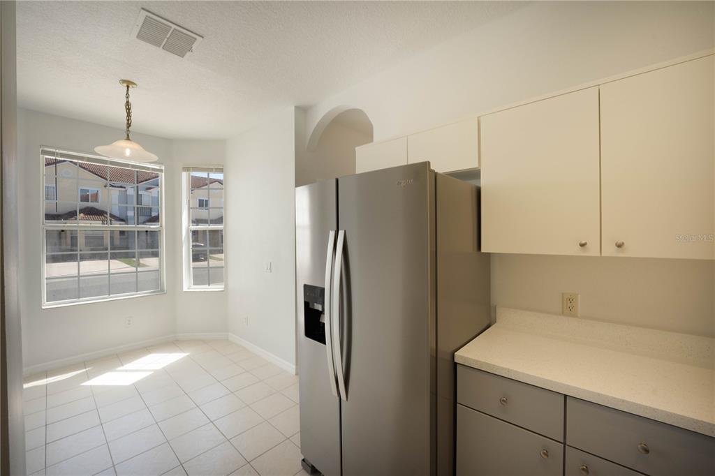A kitchen area features a stainless steel refrigerator, white upper cabinets, and a dining nook — 1241 S BEACH CIRCLE, KISSIMMEE, FL