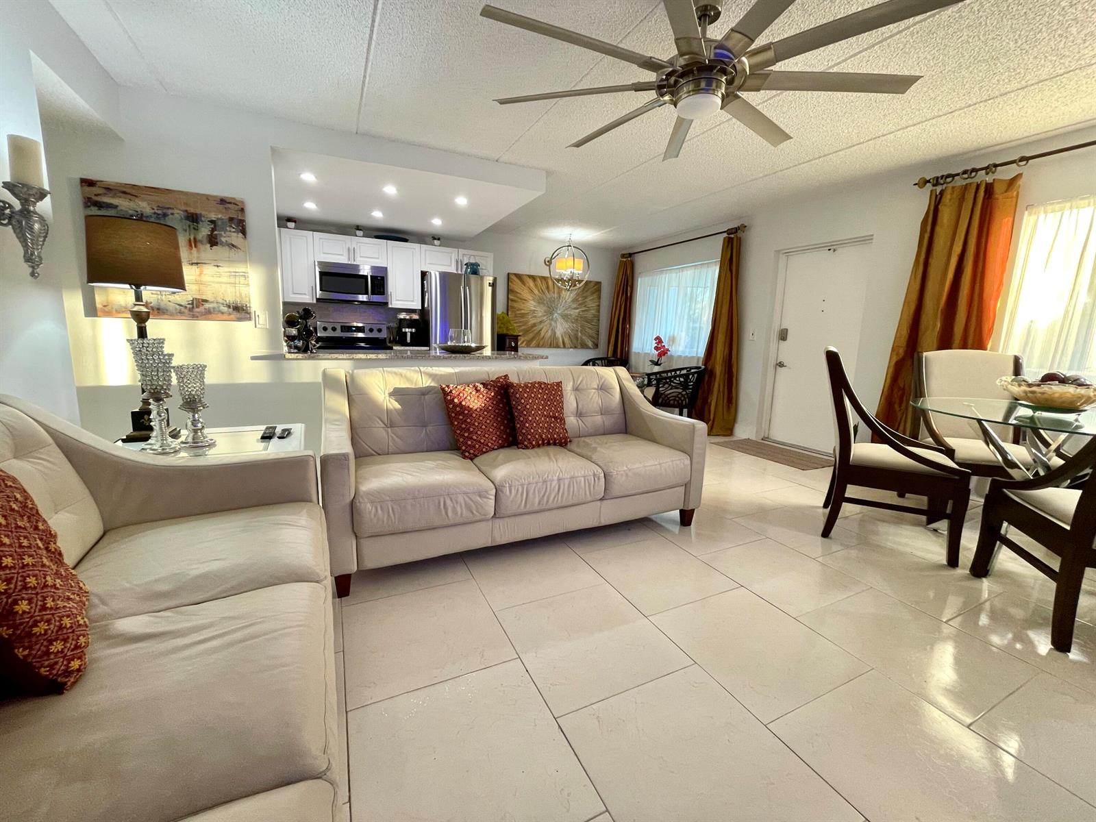 A living room with light-colored tile floors, a white sofa, and an open kitchen area — 3200 Springdale Boulevard # 107, Palm Springs FL 33461, PALM SPRINGS, FL