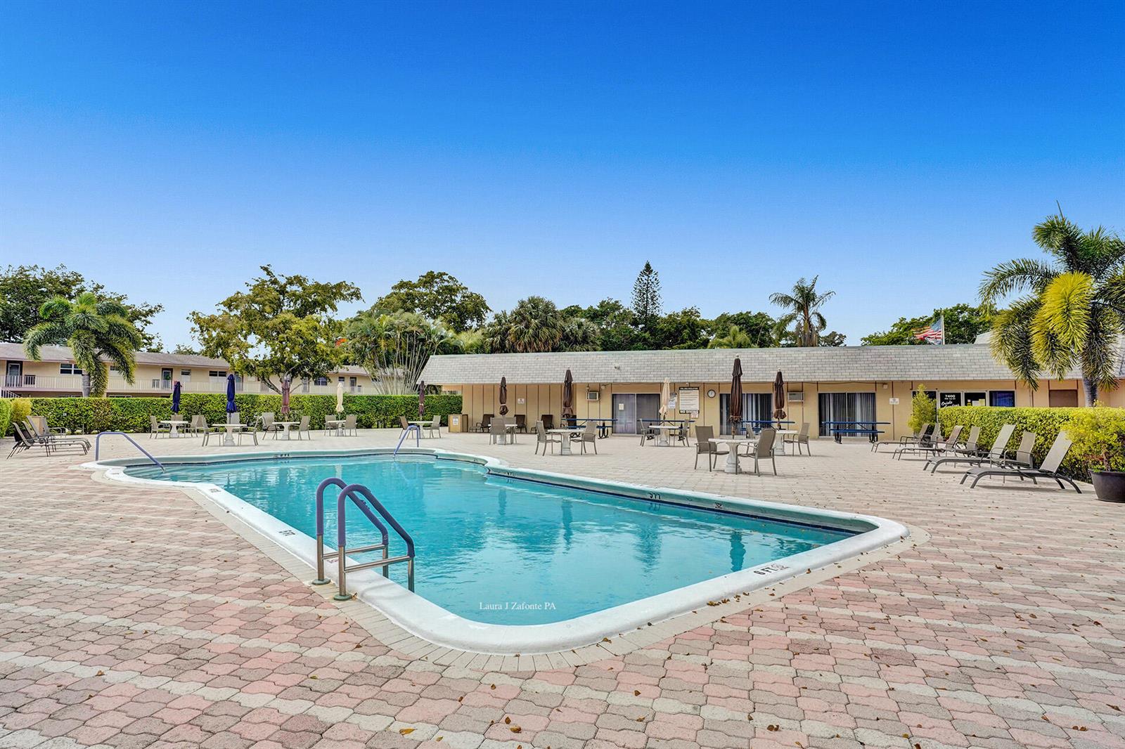 A rectangular swimming pool sits on a paved patio in front of a single-story building — 201 NW 76th Avenue # 203, Margate FL 33063, MARGATE, FL