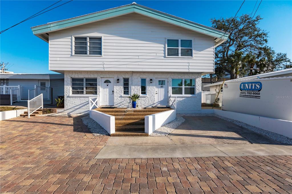 A two-story duplex with white siding and stone veneer features a central staircase and driveway — 6020 MIDNIGHT PASS ROAD UNIT 50, SARASOTA, FL
