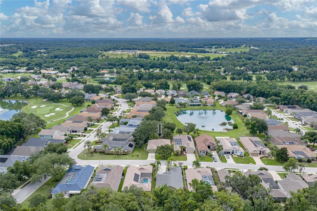 An aerial view shows a suburban neighborhood with houses, a pond, and a golf course — 12215 WOODLANDS CIRCLE, DADE CITY, FL