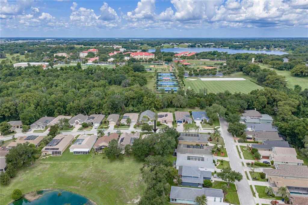 An aerial view shows a suburban neighborhood with houses, a pond, and tennis courts — 12215 WOODLANDS CIRCLE, DADE CITY, FL