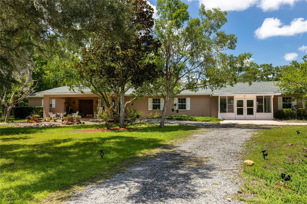 A single-story house with a gravel driveway, large trees, and a covered patio area — 11751 SE 16TH LANE, MORRISTON, FL