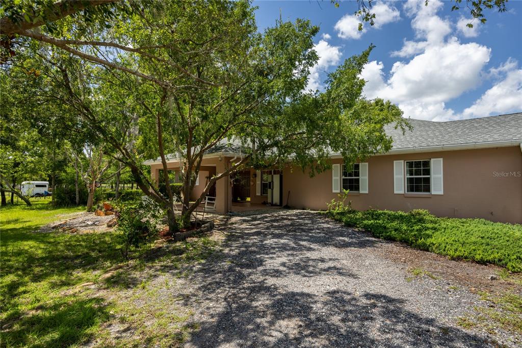 A gravel driveway leads to the front entrance and covered porch of a tan house — 11751 SE 16TH LANE, MORRISTON, FL