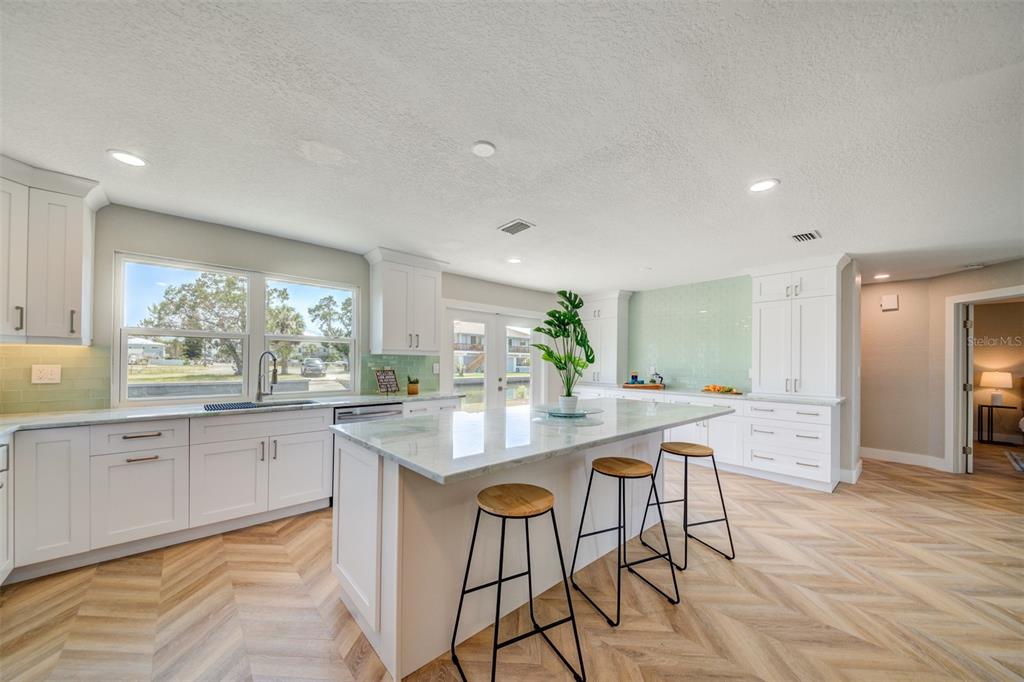 A bright kitchen features white cabinets, a marble-topped island with stools, and herringbone wood flooring — 6432 BOATYARD DRIVE, HUDSON, FL