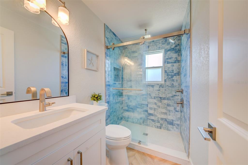 A bathroom features a white vanity, a toilet, and a walk-in shower with blue tiles — 6432 BOATYARD DRIVE, HUDSON, FL