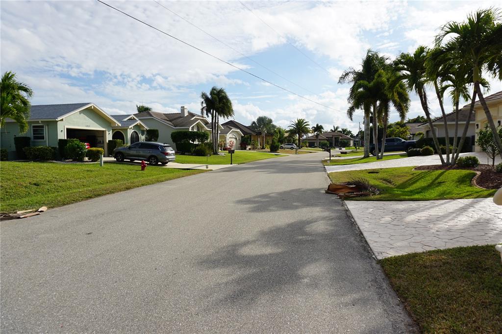 A suburban street lined with single-family homes, palm trees, and paved driveways under a cloudy sky — 4019 MALTESE COURT, PUNTA GORDA, FL