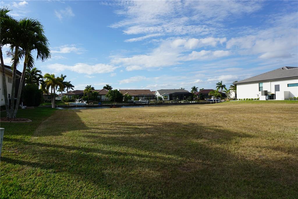 A vacant grassy lot overlooks a canal with several houses and boats in the background — 4019 MALTESE COURT, PUNTA GORDA, FL