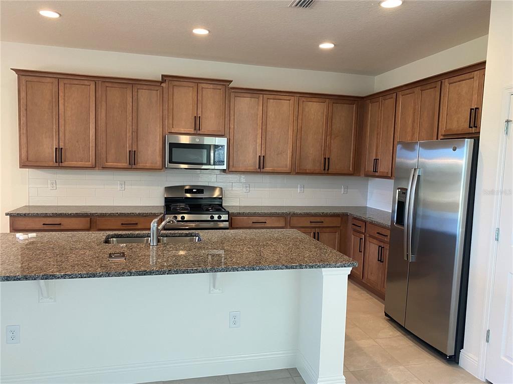 A kitchen features wood cabinets, granite countertops, stainless steel appliances, and a central island — 4842 GILDED JEWEL DRIVE, MOUNT DORA, FL