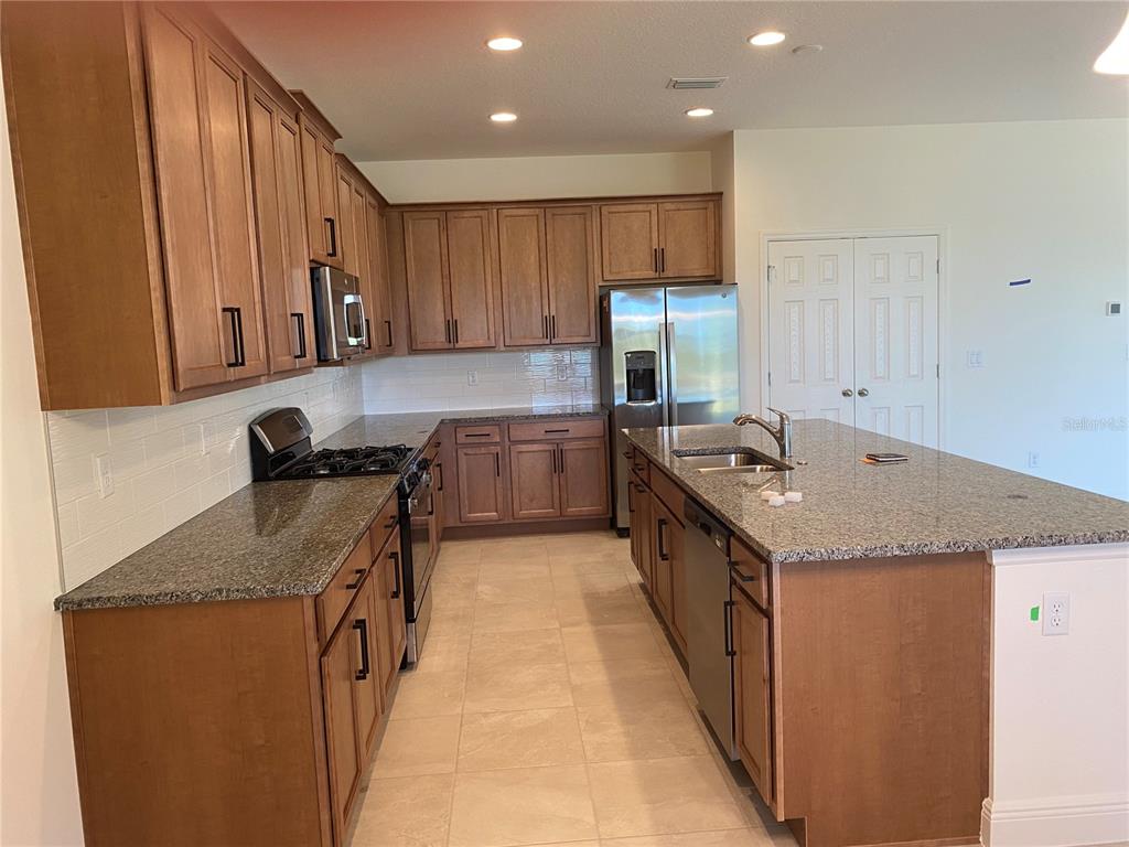 A kitchen features wood cabinets, granite countertops, a center island, and stainless steel appliances — 4842 GILDED JEWEL DRIVE, MOUNT DORA, FL