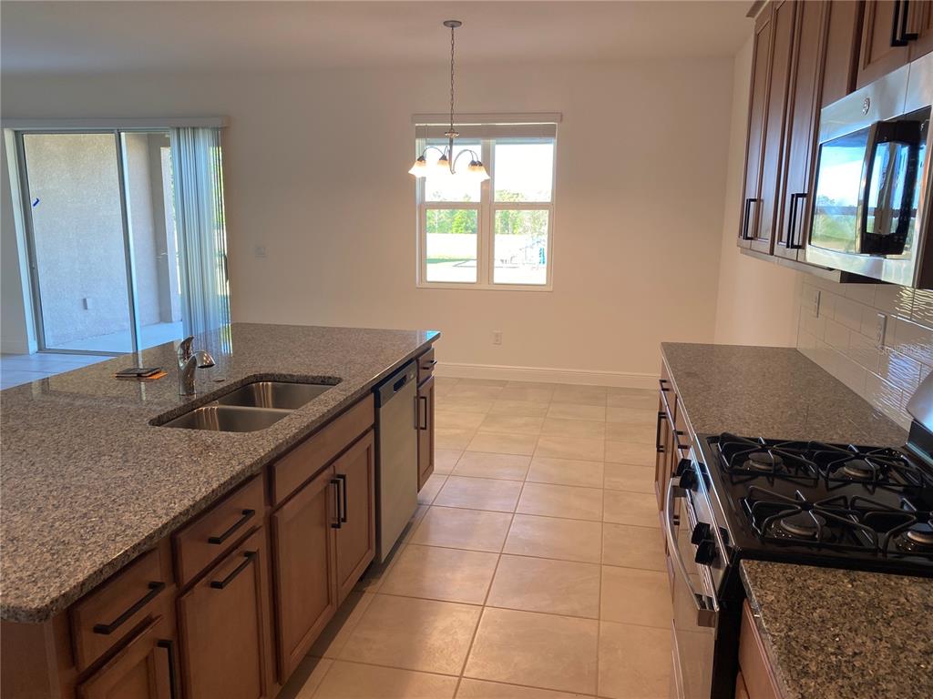 A kitchen features granite countertops, wood cabinets, a gas range, and a center island sink — 4842 GILDED JEWEL DRIVE, MOUNT DORA, FL