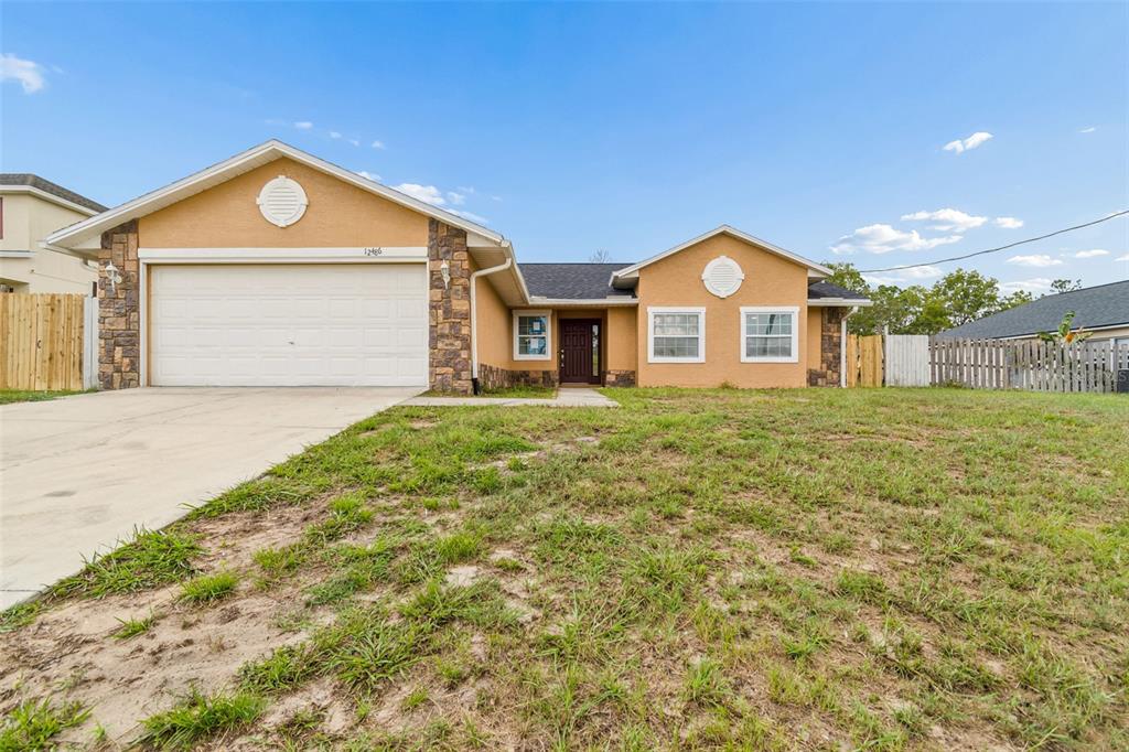 A single-story house with a tan stucco exterior, stone accents, and a two-car garage — 12486 CENTENNIAL STREET, SPRING HILL, FL