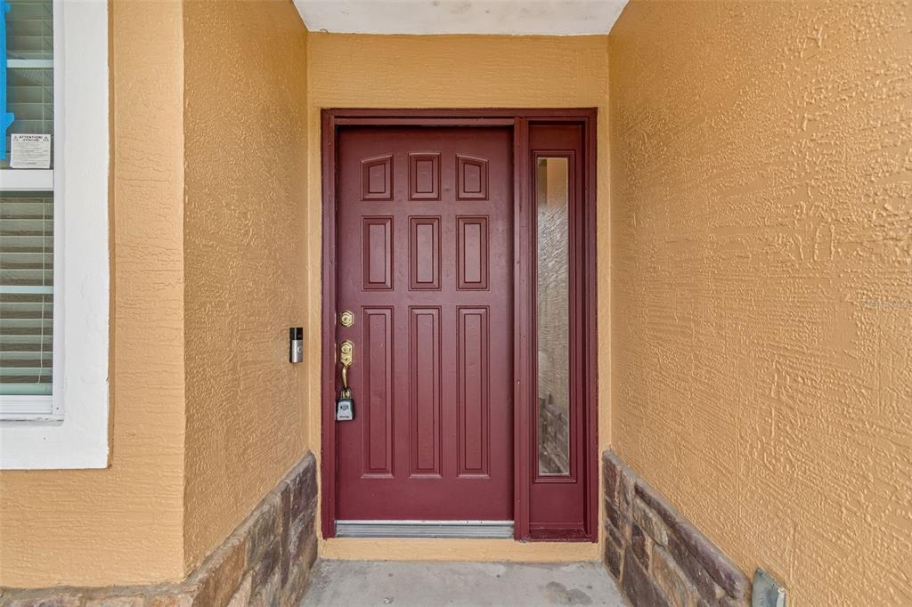A front entryway features a red six-panel door with a sidelight and stone base accents — 12486 CENTENNIAL STREET, SPRING HILL, FL