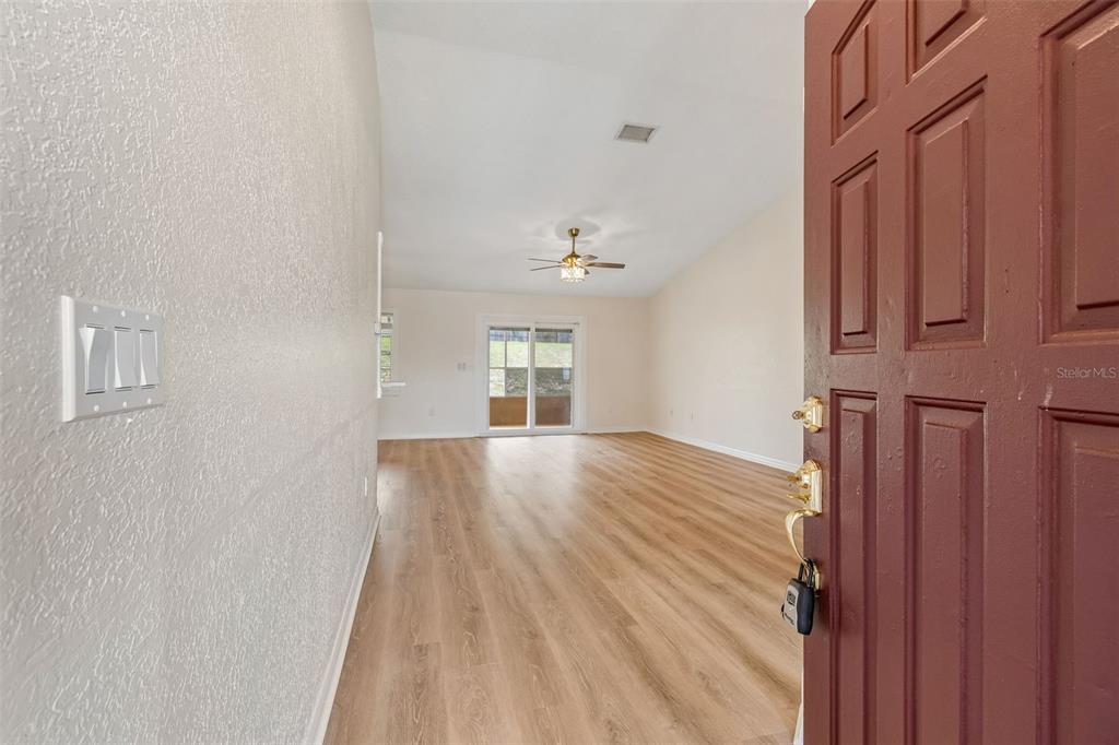 An open living area with light wood-look flooring, a ceiling fan, and a sliding glass door — 12486 CENTENNIAL STREET, SPRING HILL, FL
