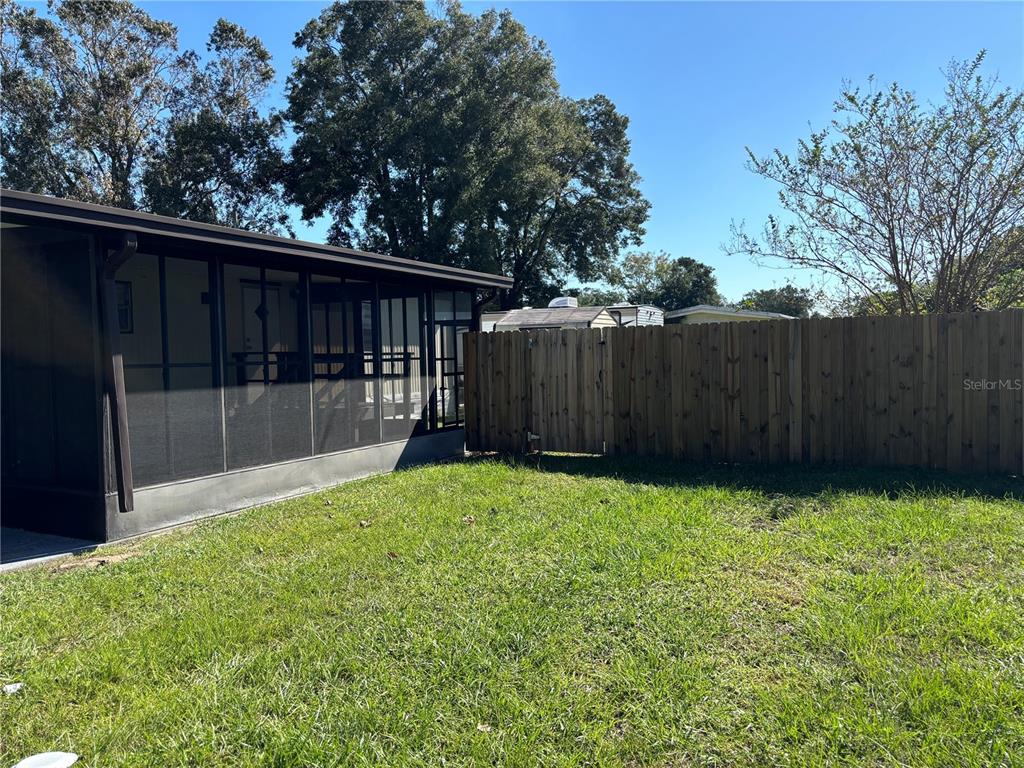 A grassy backyard features a screened-in porch attached to a house and a wooden fence — 5910 SW 63RD PLACE ROAD, OCALA, FL