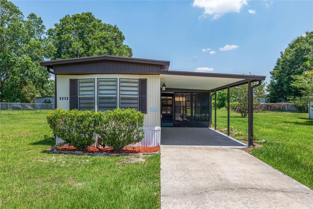 A single-story manufactured home features a front carport, a bay window, and a grassy yard — 5910 SW 63RD PLACE ROAD, OCALA, FL