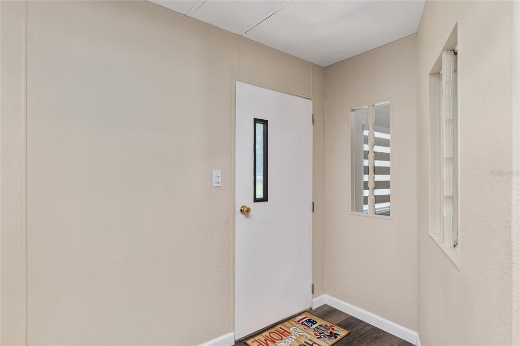 An entryway features a white door with a vertical window, beige walls, and wood flooring — 5910 SW 63RD PLACE ROAD, OCALA, FL