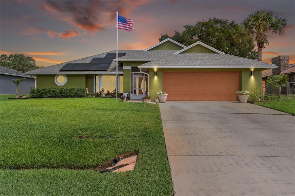 A green single-story house with a two-car garage, a flagpole, and solar panels on the roof — 185 JOY HAVEN DRIVE, SEBASTIAN, FL