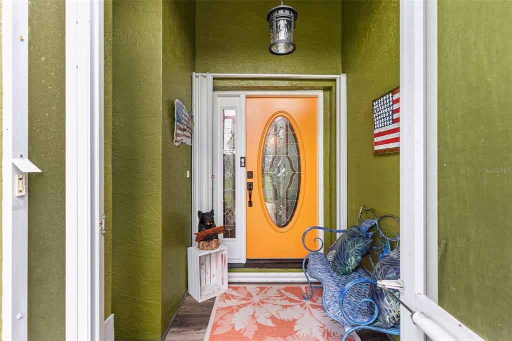 An entryway features olive green walls, an orange front door, and a blue metal bench — 185 JOY HAVEN DRIVE, SEBASTIAN, FL