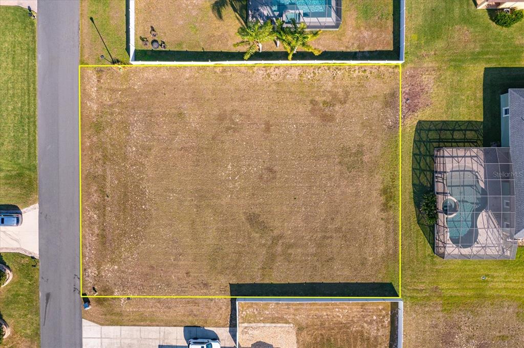 An aerial view shows a vacant, rectangular residential lot outlined in yellow between two houses — 1013 MYRTLE BREEZES COURT, FRUITLAND PARK, FL