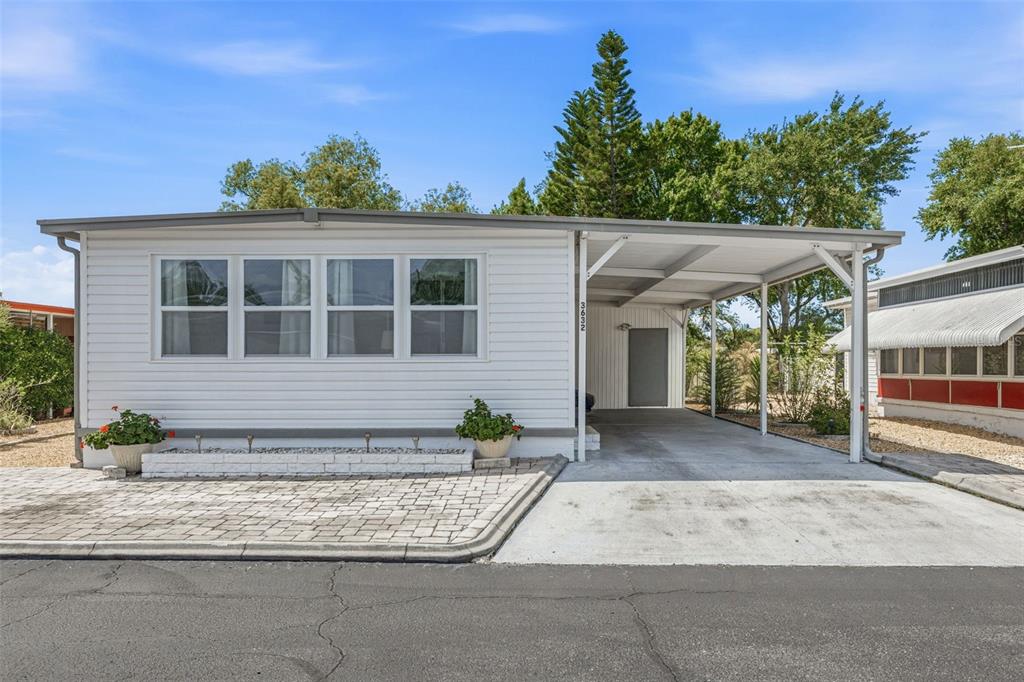 A white mobile home features a carport, a paved driveway, and a small front garden bed — 3632 TIKI DRIVE, HOLIDAY, FL