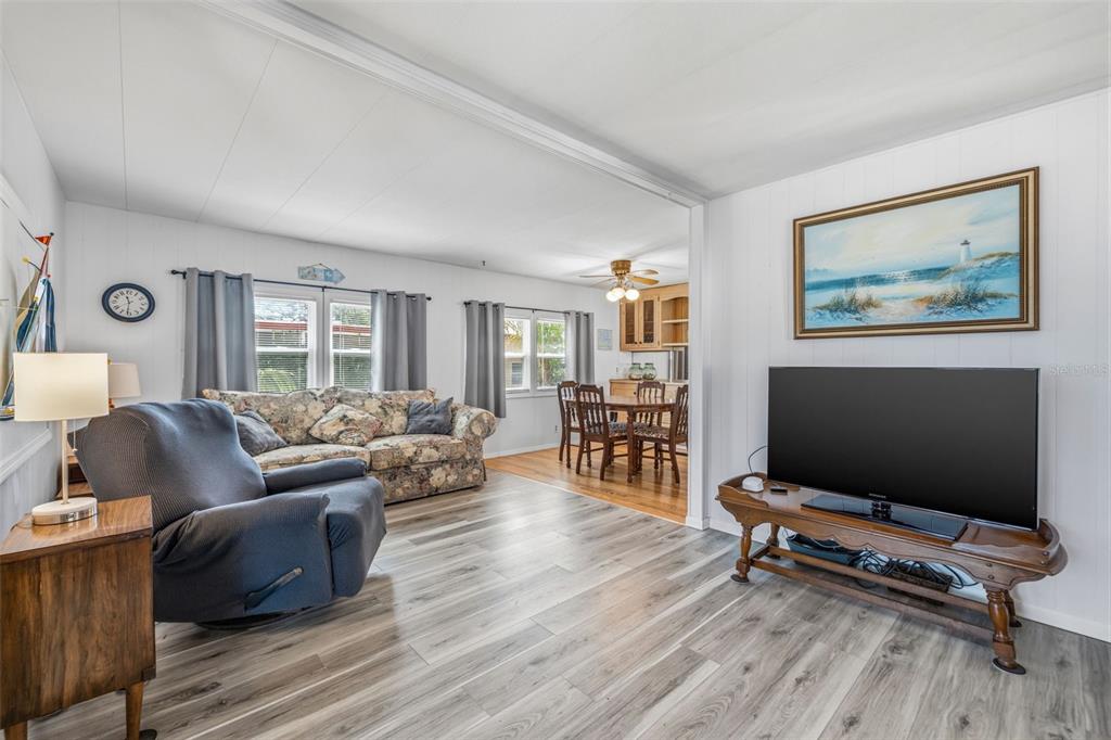A living room with wood-look flooring, a floral sofa, a recliner, and a dining area — 3632 TIKI DRIVE, HOLIDAY, FL