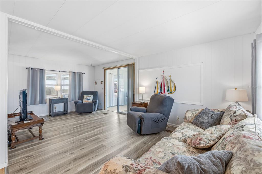 A living room features wood-look flooring, a floral sofa, two recliners, and a sliding glass door — 3632 TIKI DRIVE, HOLIDAY, FL