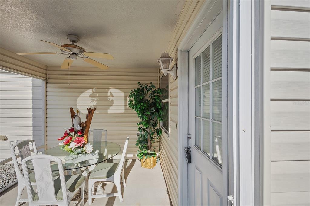 A covered patio features a glass-top dining set, a ceiling fan, and a white door — 2343 PINE RIDGE STREET, THE VILLAGES, FL
