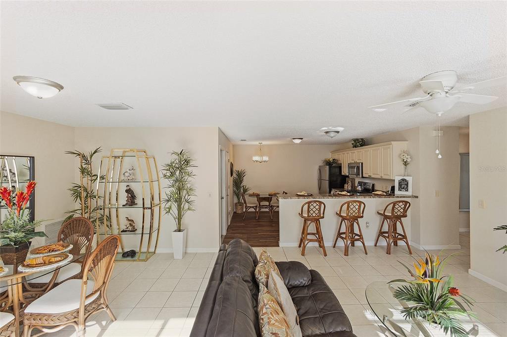 An open-concept living and dining area features tile floors, a kitchen bar, and wicker furniture — 2343 PINE RIDGE STREET, THE VILLAGES, FL