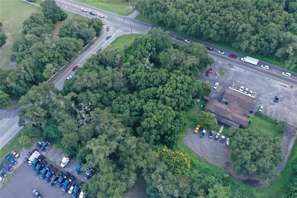 An aerial view shows a commercial building, a parking lot with trucks, and dense trees — 24439 SORRENTO AVENUE, SORRENTO, FL