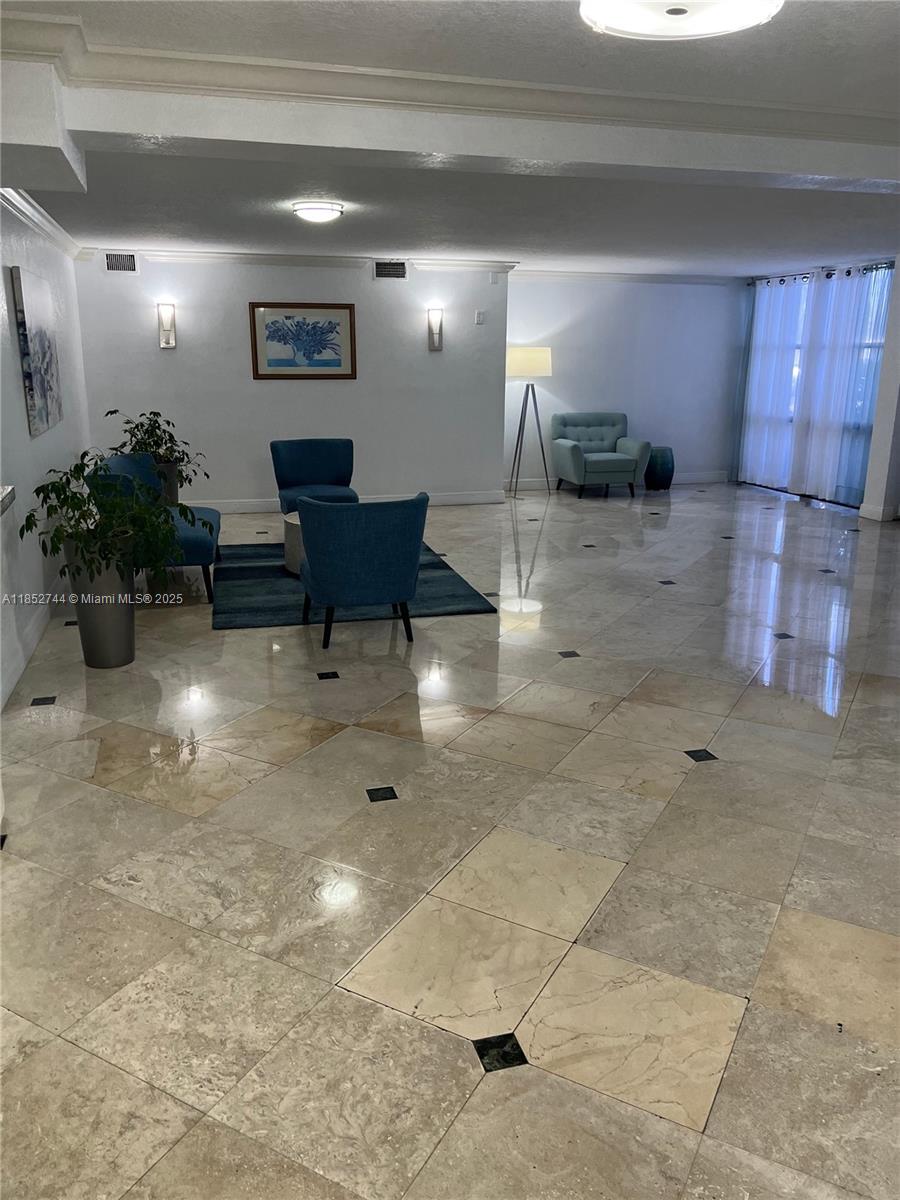 A spacious lobby features polished marble tile flooring, blue accent chairs, and recessed lighting — 1000 Parkview Dr # 523, Hallandale Beach FL 33009, HALLANDALE BEACH, FL