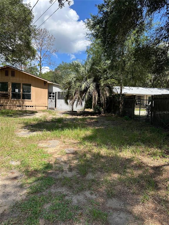 A tan house and a small storage shed sit on a grassy lot under trees — 1968 SE 161ST TERRACE, OCKLAWAHA, FL