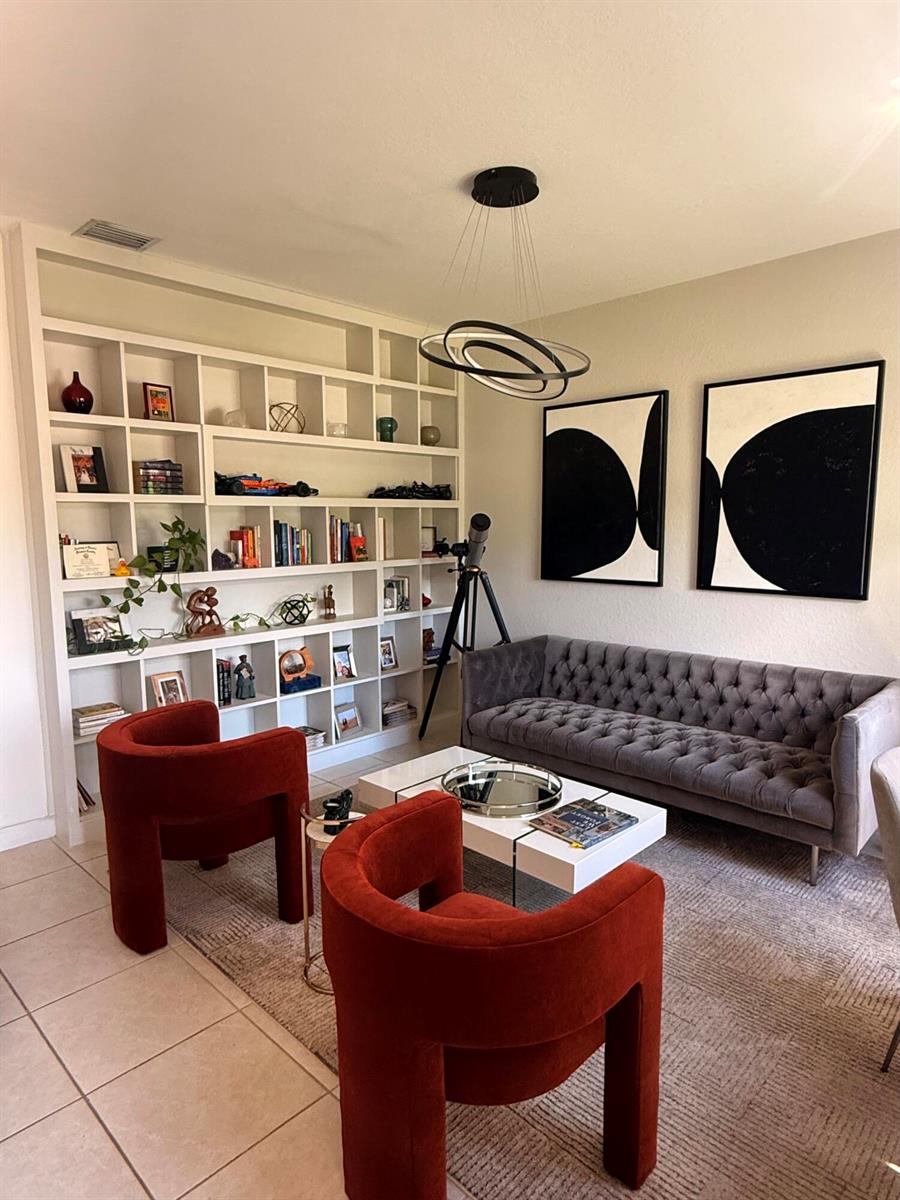 A living room features a built-in bookshelf, a grey tufted sofa, and two red chairs — 21423 NE 2nd Place, Miami FL 33179, MIAMI, FL