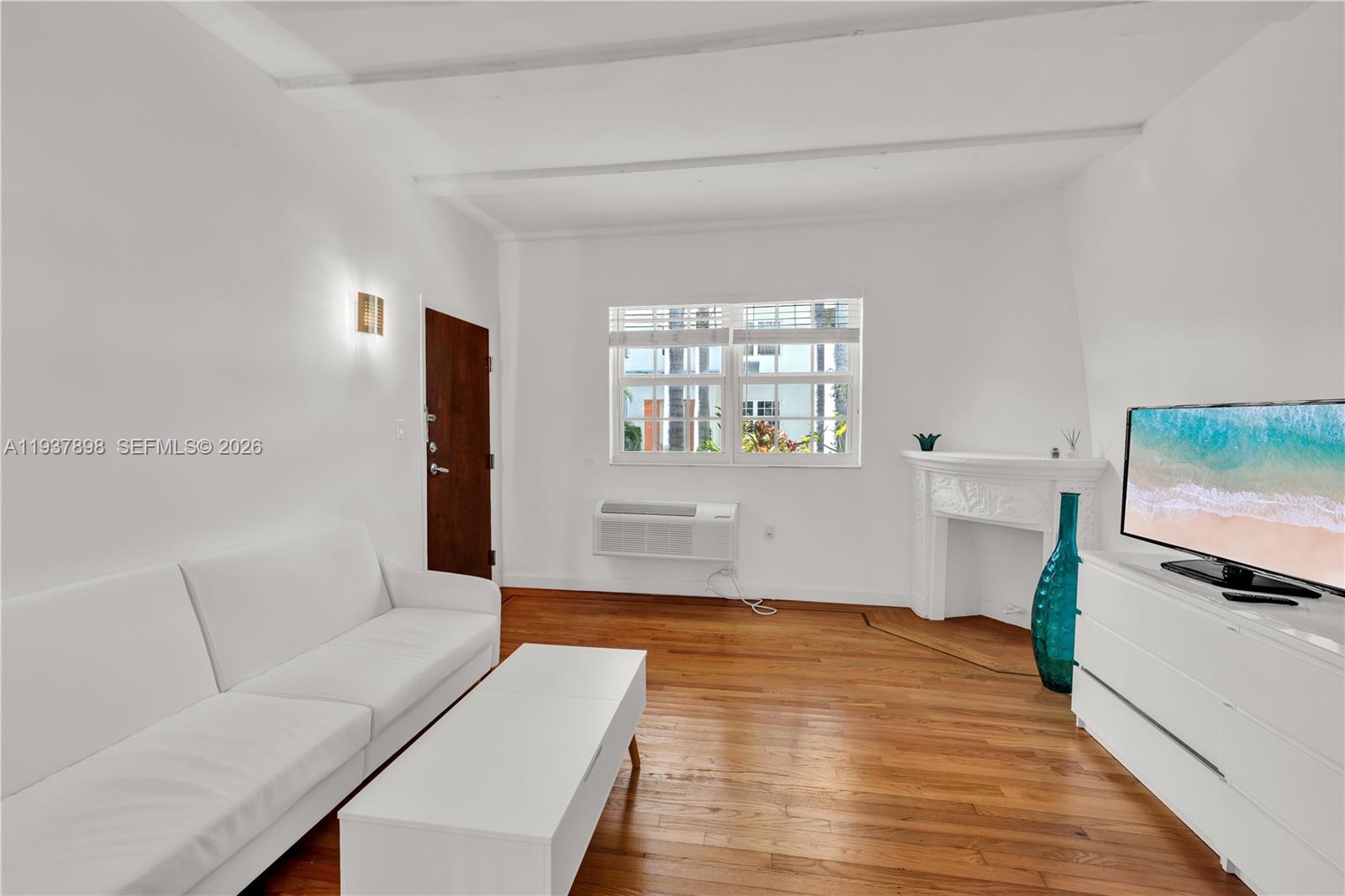 A living room features white walls, hardwood floors, a white sofa, and a fireplace — 439 15th St # 2, Miami Beach FL 33139, MIAMI BEACH, FL