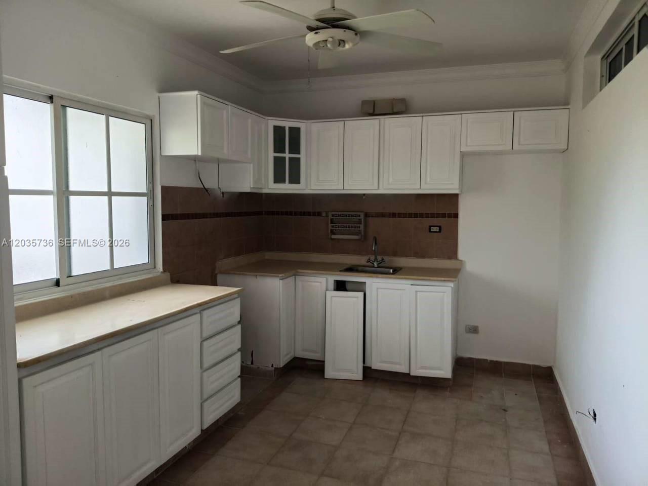 A kitchen features white cabinets, a brown tiled backsplash, and a ceiling fan — 1 Punta cana # 0, FL, FL