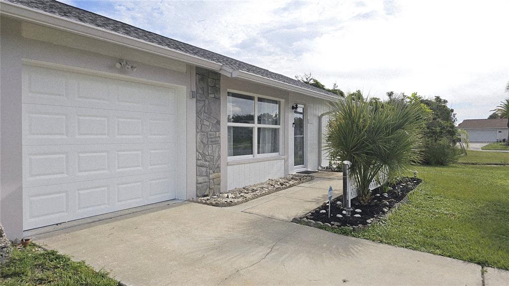 A single-story house with a white garage door, stone accent wall, and a concrete driveway — 13398 BALLON AVENUE, PORT CHARLOTTE, FL