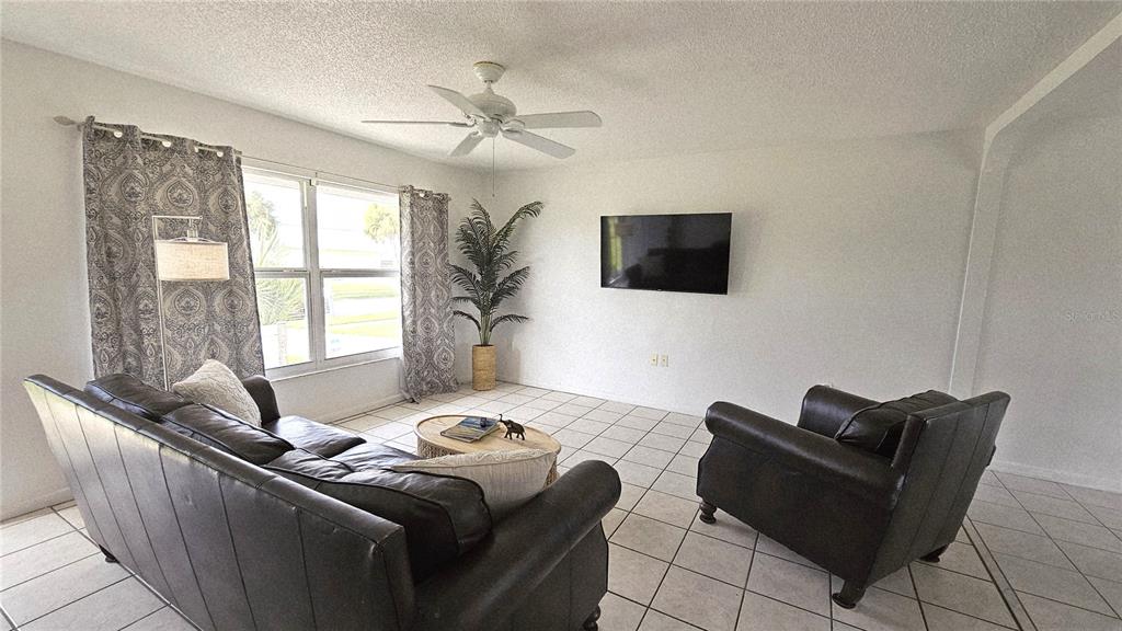 A living room features a leather sofa, armchair, wall-mounted television, and tile flooring — 13398 BALLON AVENUE, PORT CHARLOTTE, FL