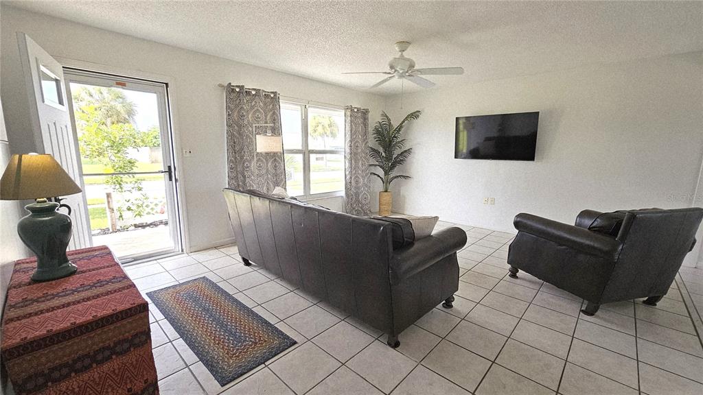 A living room features white tile floors, a dark leather sofa, and a wall-mounted television — 13398 BALLON AVENUE, PORT CHARLOTTE, FL
