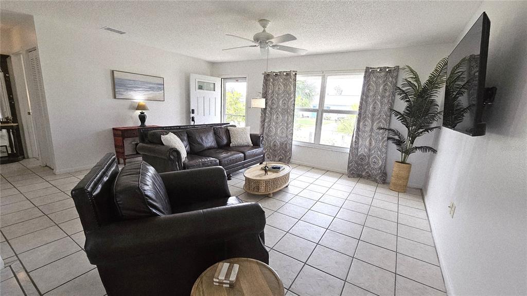A living room features tile flooring, a leather sofa and armchair, and a wall-mounted television — 13398 BALLON AVENUE, PORT CHARLOTTE, FL