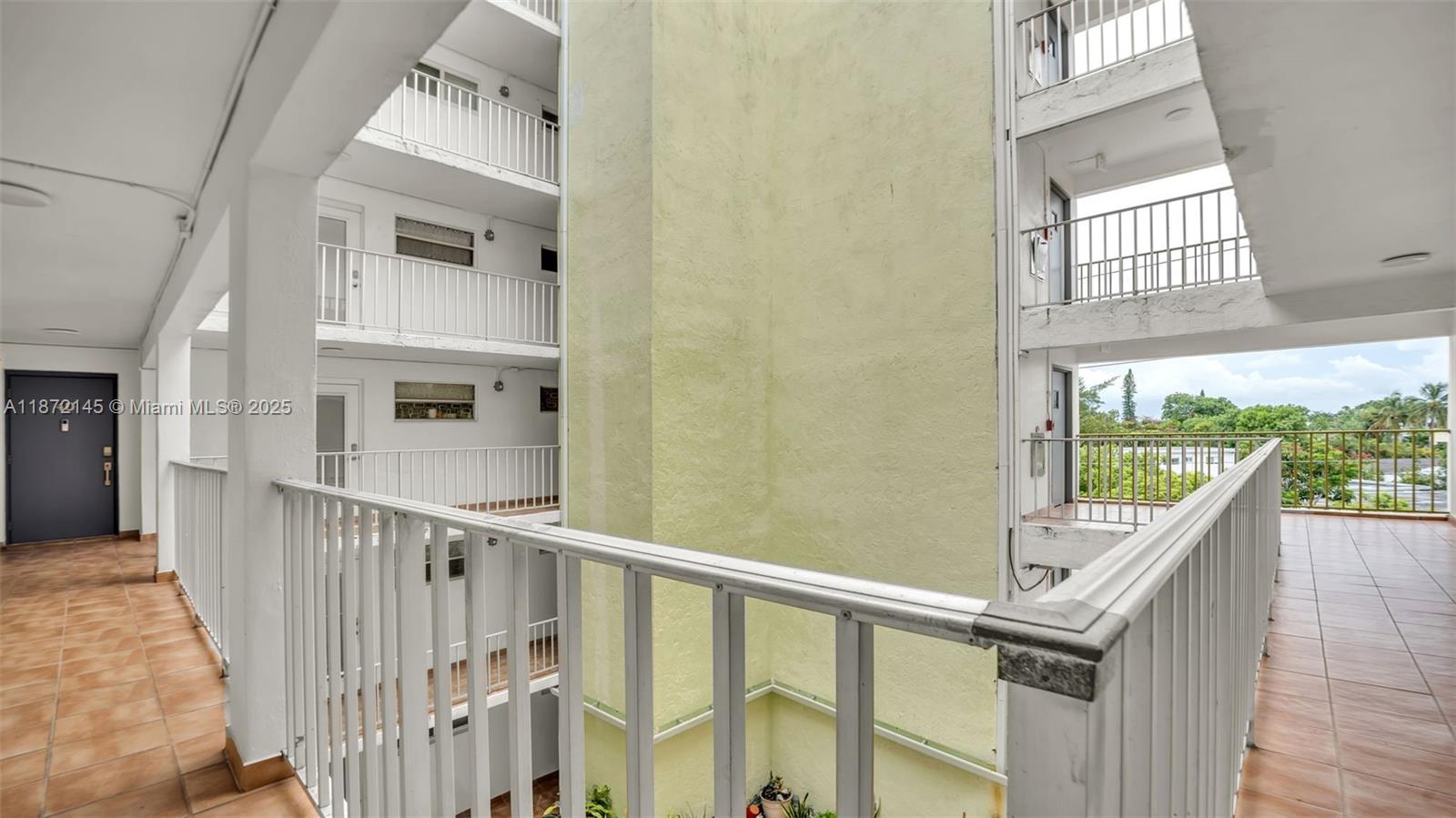 An open-air apartment building corridor features white railings, tiled floors, and a central light-colored pillar — 8001 Crespi Blvd # 4B, Miami Beach FL 33141, MIAMI BEACH, FL