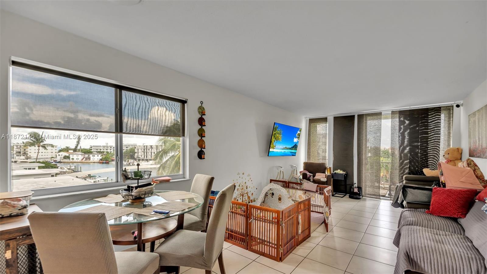 A living and dining area with tile floors, a glass table, and a balcony view — 8001 Crespi Blvd # 4B, Miami Beach FL 33141, MIAMI BEACH, FL